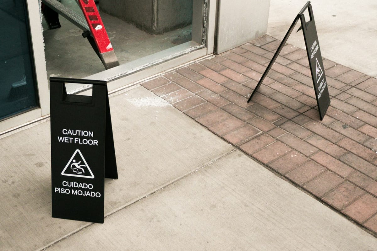 Bilingual wet floor caution signs on the walkway outside a business entrance